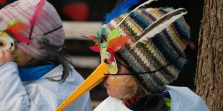 Zwei Kinder mit bunten selbstgebastelten Vogelmasken auf dem Kopf.