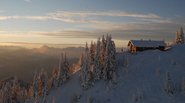 Blick vom Garlandhang am Brauneck in Richtung Süden auf die verschneiten Alpen bei aufgehender Sonne.